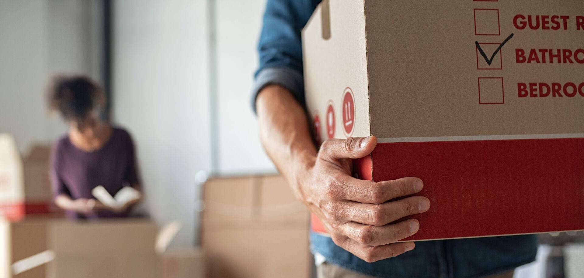 Senior couple sitting on a cozy couch in a bright, modern living room, looking happy and relaxed. The decor features soft, neutral colors and natural light streaming through large windows, symbolizing the benefits of downsizing.