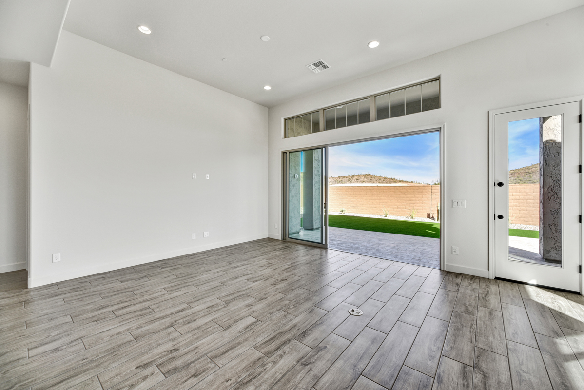 Bright and spacious living room in a new construction home in Peoria, Arizona, featuring large energy-efficient windows that let in ample natural light, neutral-tone walls, and modern tile flooring. The open-concept layout seamlessly connects the living area to the kitchen, creating a welcoming and versatile space perfect for relaxation or entertaining.