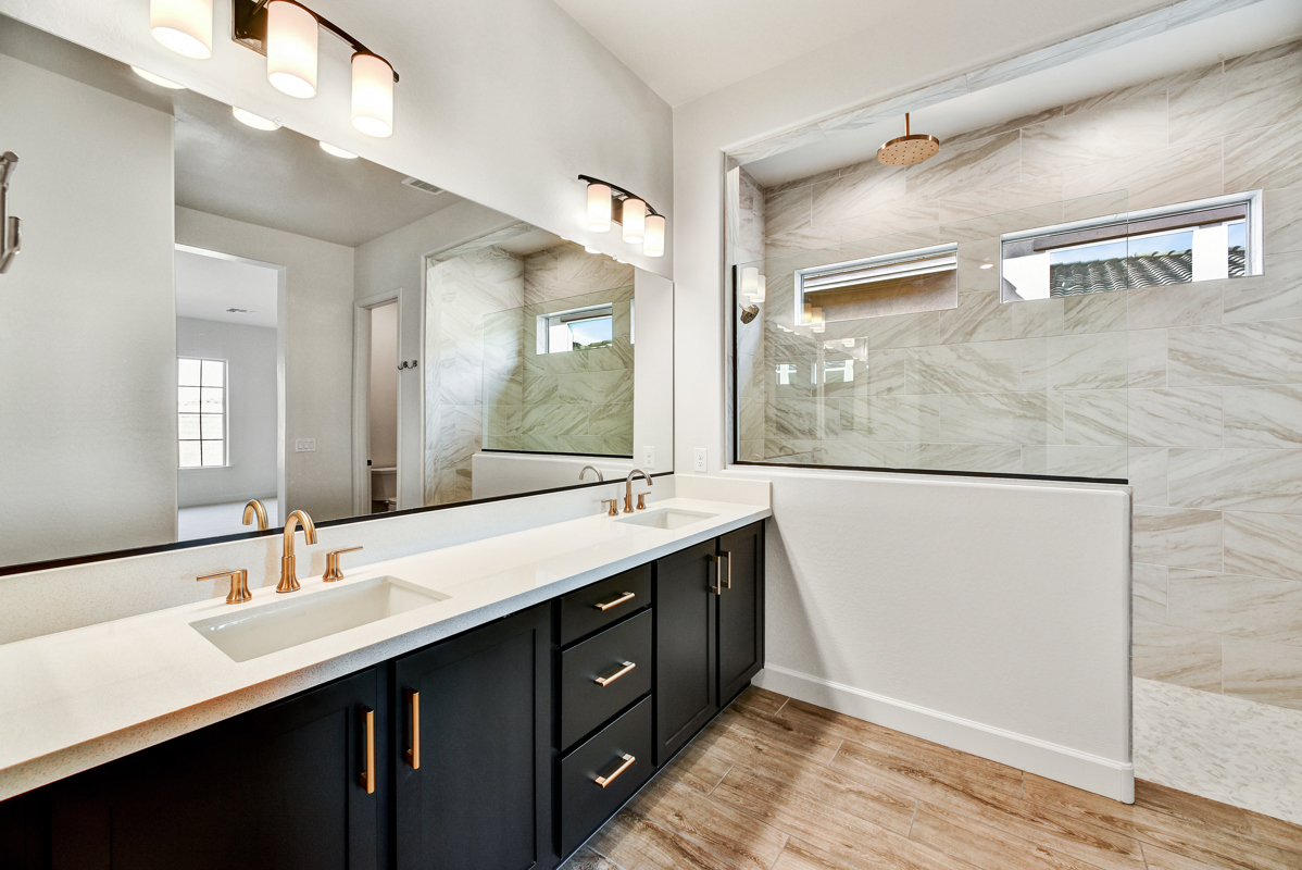 Luxurious primary bathroom in a new construction home in Peoria, Arizona, featuring a spacious walk-in shower with custom subway tile, dual quartz vanities, and sleek modern fixtures. The spa-like design creates a serene and relaxing atmosphere, perfect for unwinding after a long day.