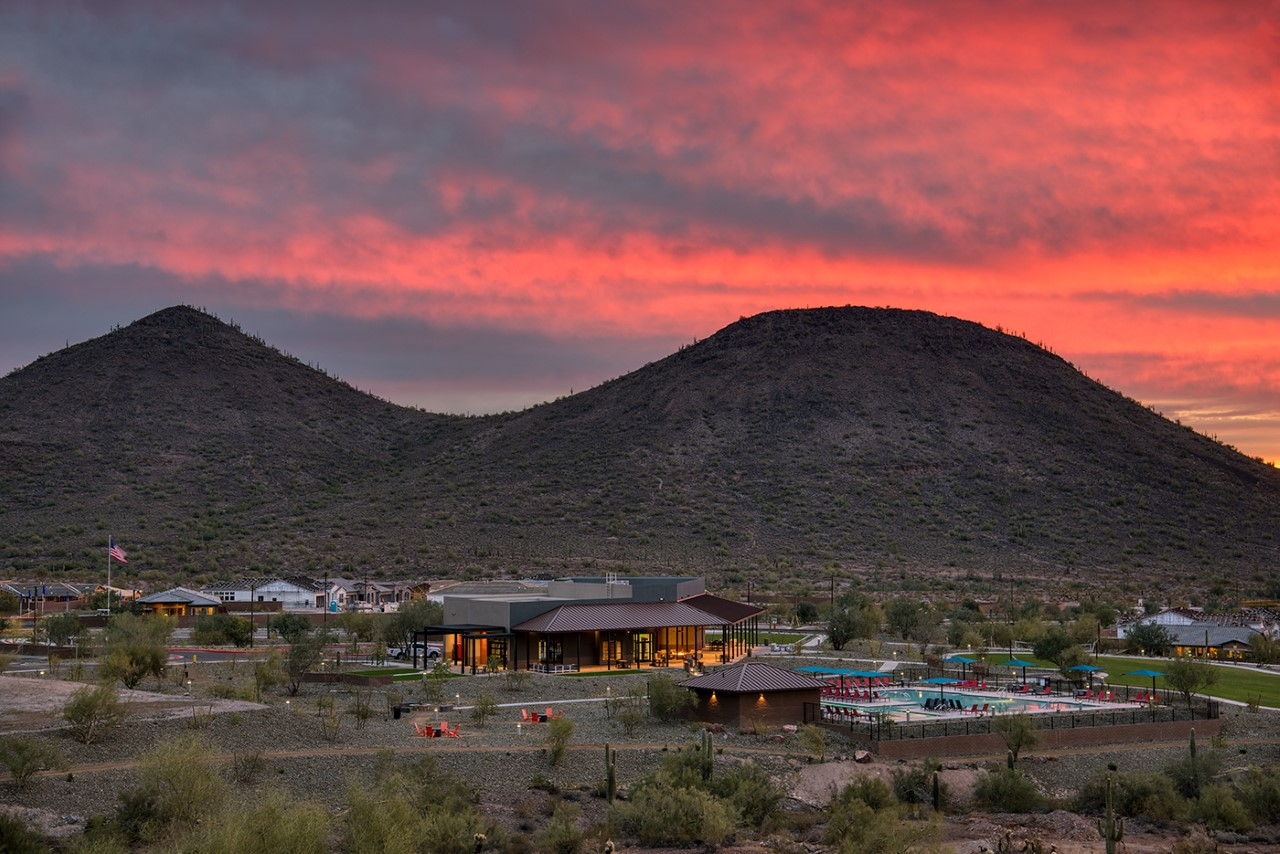 Scenic view of the Northpointe community in Peoria, AZ, set against a stunning desert landscape with vibrant sunset skies. The image highlights the community’s modern amenities, including a clubhouse, pool, and recreational spaces, surrounded by serene natural beauty and mountain views, showcasing an ideal blend of luxury and outdoor living.