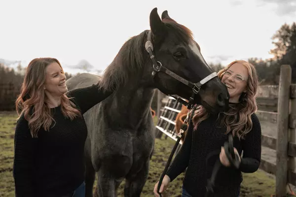 Female farm realtors on Vancouver Island getting kissed by a horse