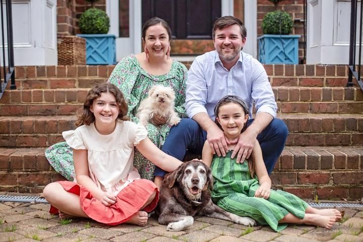 A family sitting on the steps of a house with a dogDescription automatically generated