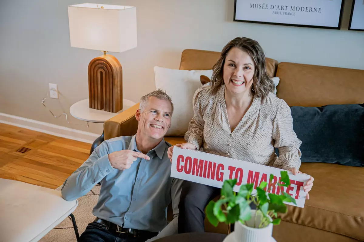 Jeff and Karen sit together with a red and white sign that says 'Coming to Market'