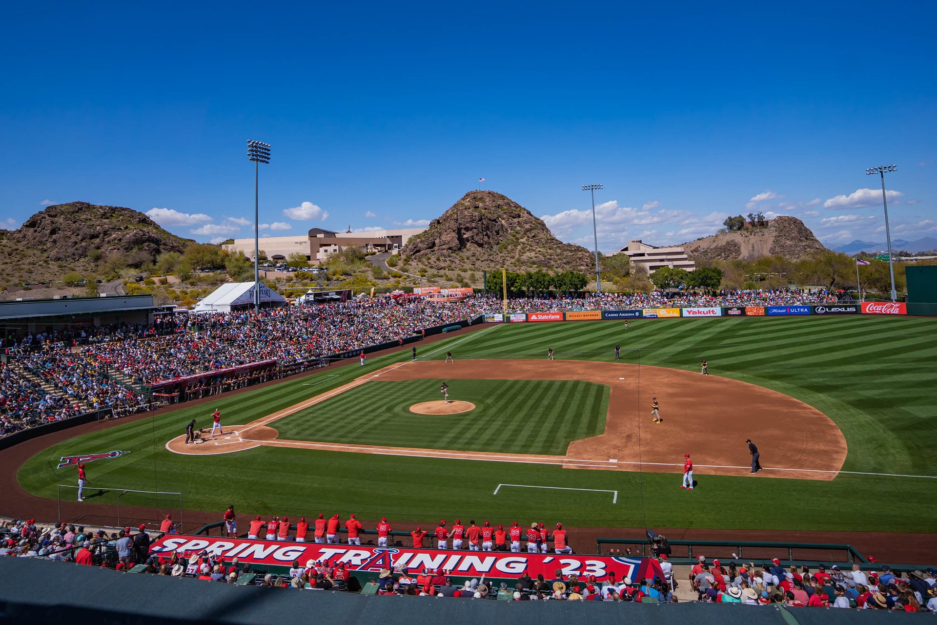 Spring training baseball game at Tempe Diablo Stadium in Tempe, Arizona, with a packed crowd, scenic desert hills in the background, and clear blue skies, showcasing Tempe as a popular destination for baseball fans and spring events.