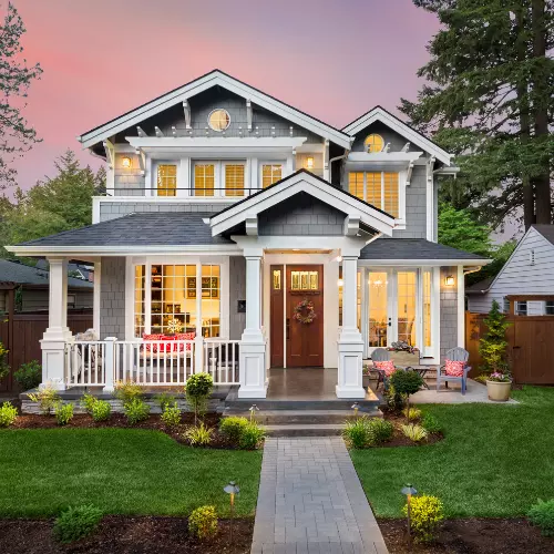 Gray residential home with lights on and a lush green yard