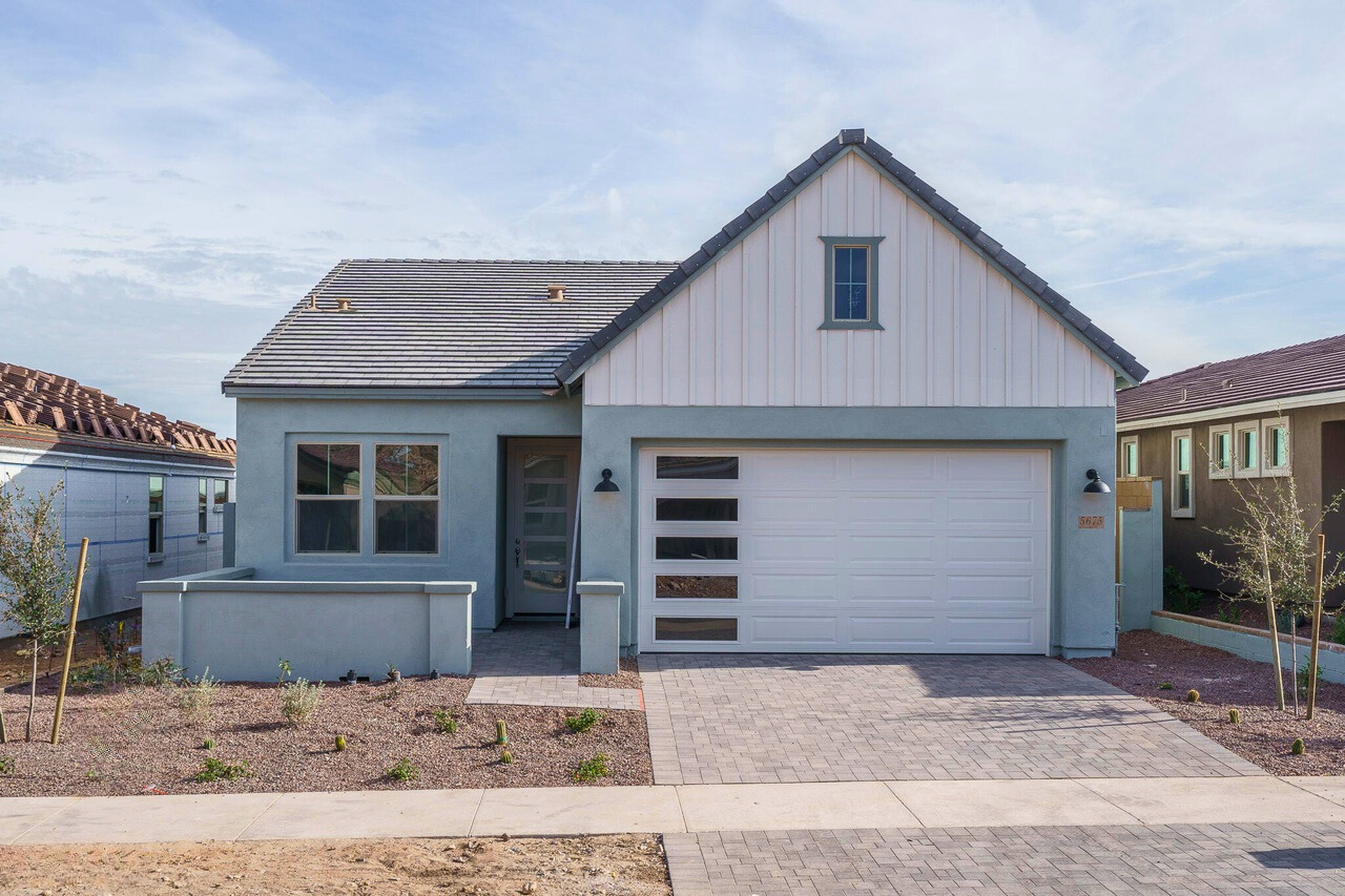 Newly constructed modern farmhouse-style home at Victory at Verrado in Buckeye, Arizona, featuring a clean, minimalistic exterior with a two-car garage, desert landscaping, and energy-efficient design, perfect for active adults seeking a vibrant 55+ community.