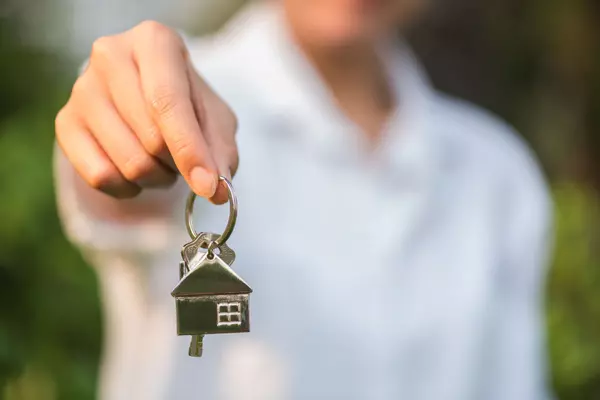 house key in woman hand and green leaves background