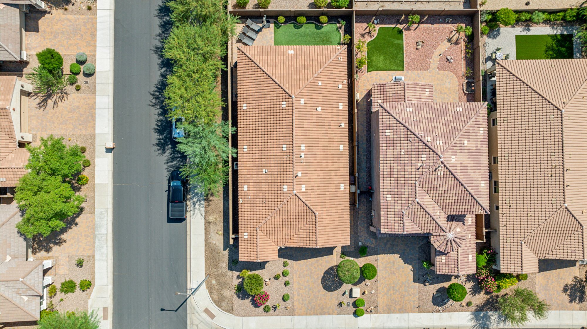 Aerial view of a well-maintained home in Vistancia, Peoria, AZ, showcasing a spacious backyard with pavers and turf, a three-car tandem garage, and proximity to scenic desert landscapes within the master-planned community.