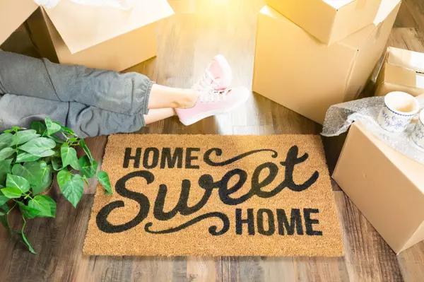 Woman Wearing Sweats Relaxing Near Home Sweet Home Welcome Mat, Moving Boxes and Plant