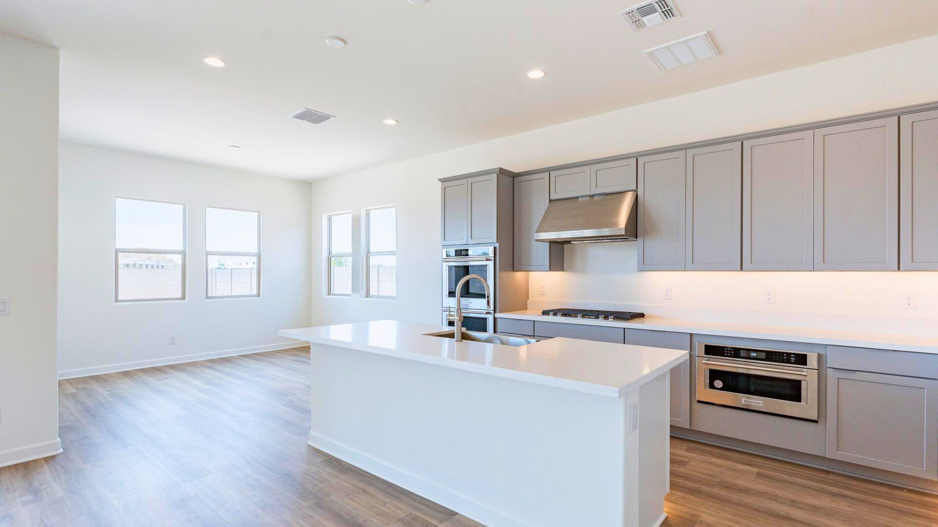 Modern gourmet kitchen in The Preserve at San Tan featuring two-toned cabinets, quartz countertops, a large island, upgraded Kitchen Aid appliances, and under-cabinet lighting.