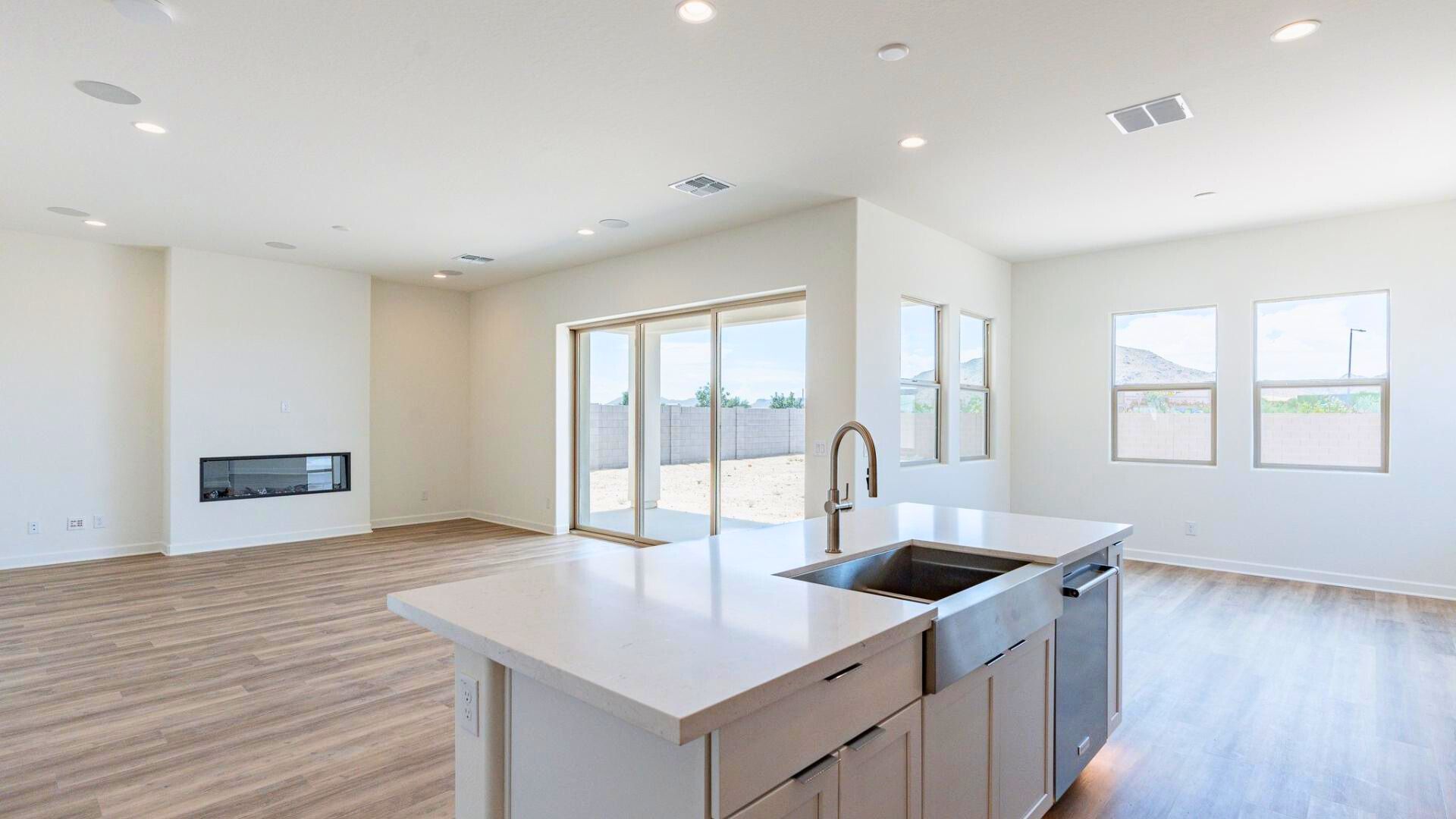 View from the modern kitchen into the spacious living room, featuring a built-in fireplace and large sliding glass doors that open to a covered patio, offering seamless indoor-outdoor living in The Preserve at San Tan.