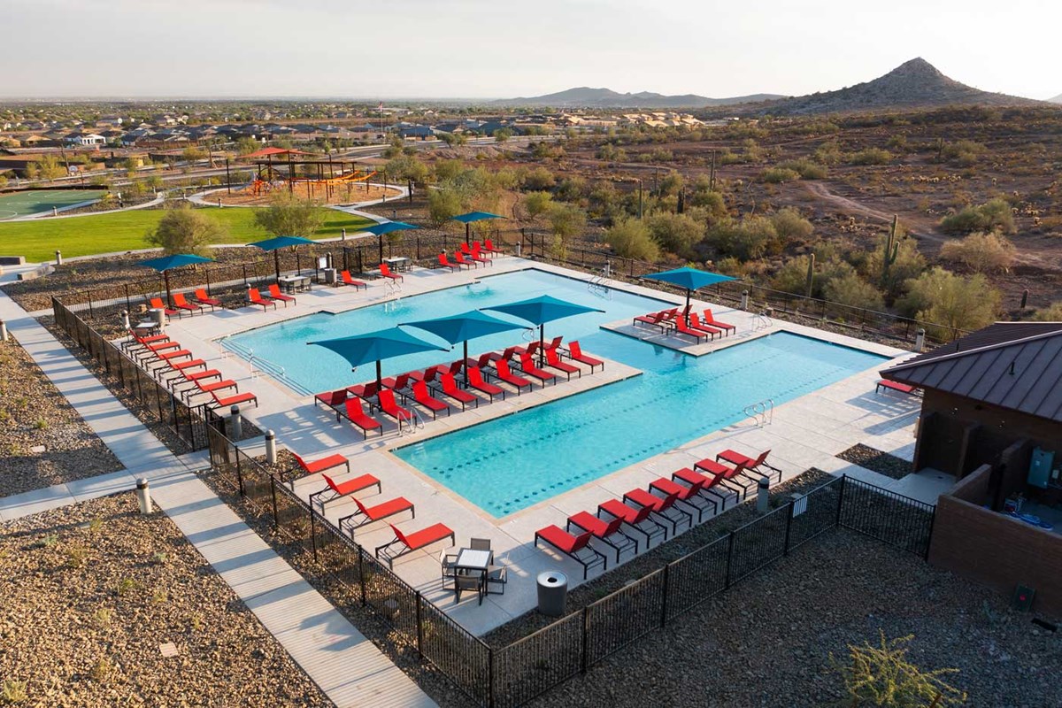 Alt text: "A resort-style pool at Vistancia in Peoria, AZ, featuring crystal-clear water, palm trees, and lounge chairs surrounding the pool area. The setting is serene with blue skies and well-maintained landscaping, offering a luxurious and relaxing atmosphere for residents and visitors.