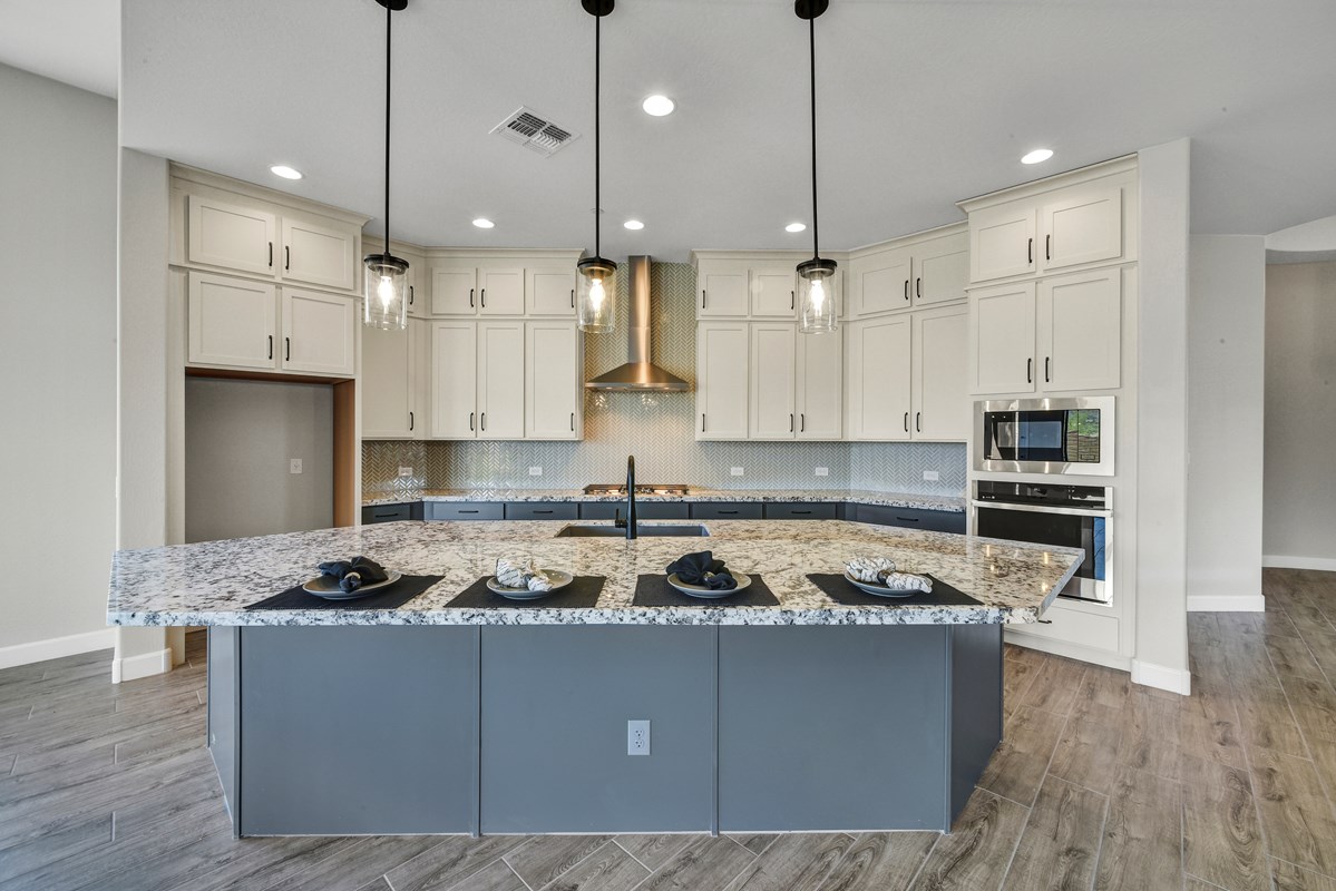 A modern kitchen featuring slate blue lower cabinets and white upper cabinets, complemented by sleek quartz countertops. The gourmet kitchen design includes wood-look tile floors, adding warmth and texture to the space.