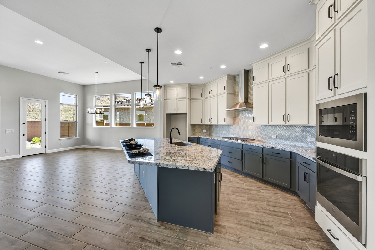 A modern gourmet kitchen featuring slate blue lower cabinets and white upper cabinets. The kitchen is equipped with sleek quartz countertops and a stylish wood-look tile floor, creating a contemporary yet warm atmosphere.