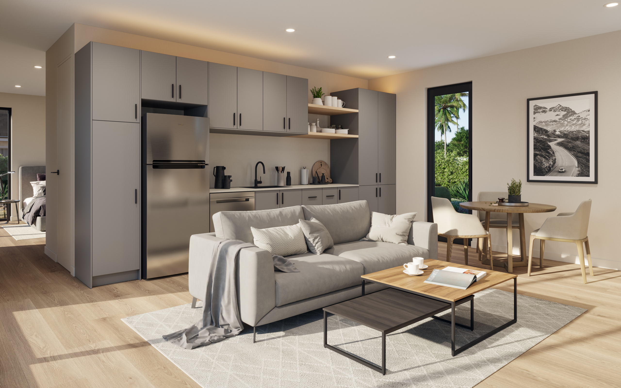 Spacious living room and kitchen in an Arizona ADU featuring modern grey cabinetry, stainless steel appliances, and light wood flooring. The living area includes a comfortable grey sofa with neutral decor and a wooden coffee table, while the dining nook has a round table with chairs near a large window overlooking desert landscaping. The kitchen is equipped with ample storage, a built-in fridge, and minimalist design elements, creating a sleek and functional living space that blends style and practicality.