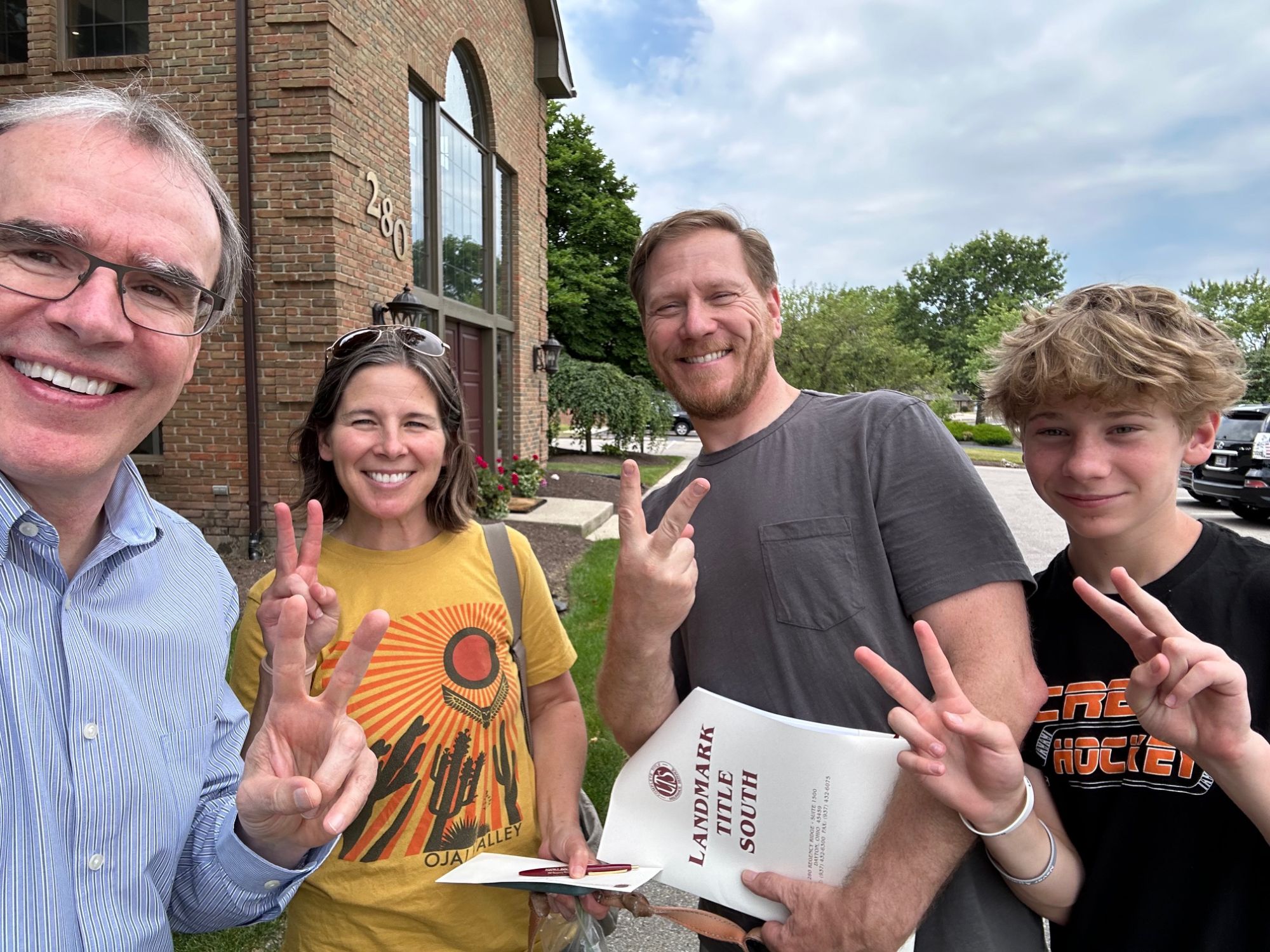 Two happy clients from Beavercreek, OH stand besides their son and David Campbell, Realtor. They're all looking towards the camera, smiling and holding up two fingers.
