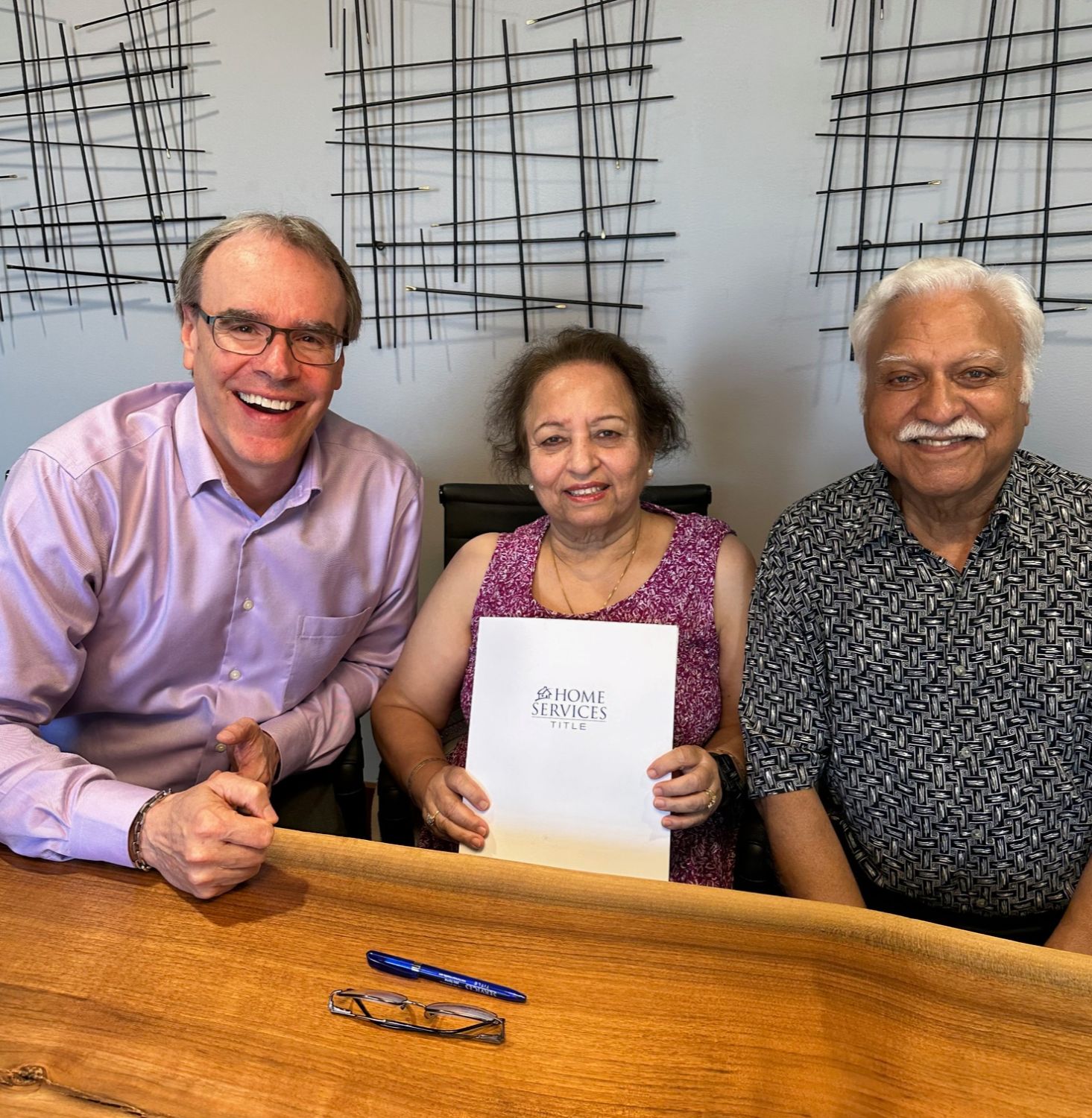 David Campbell smiling besides a couple holding a folder that reads "Home Services Title"