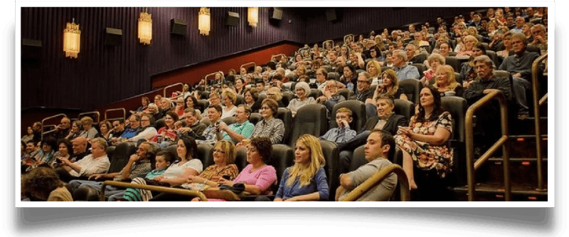 Full movie theater audience seated in rows of dark chairs.