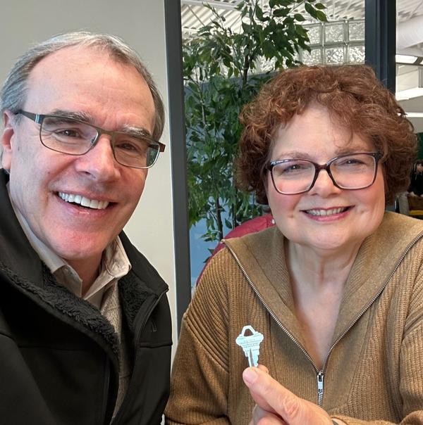 David Campbell Realtor stands to the right of a woman holding a house key - they are both smiling towards the camera.