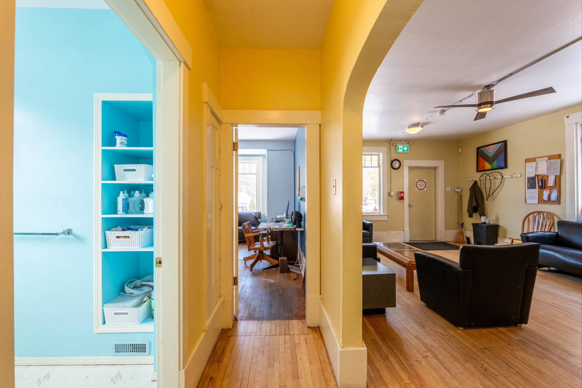 Interior view of 818 Vernon Street, Nelson BC, showing a bright hallway leading to an office space and a welcoming reception or lounge area. The space features hardwood floors, large windows for natural light, and a functional layout with multiple rooms.